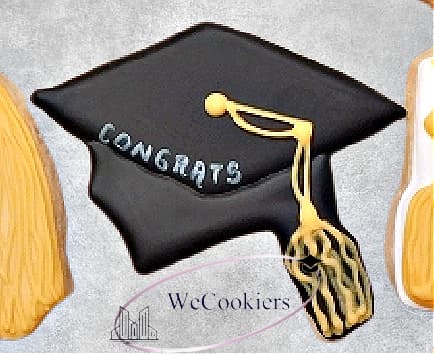 This image shows the results of using a white food color marker on decorated sugar cookies. The picture is of a graduation cap with the word 'congrats' written in white.