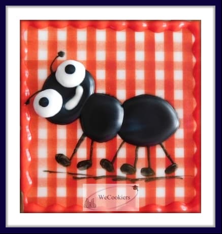 This image reflects an ant walking over a red and white plaid picnic cloth, smiling. It shows the royal icing shiny and puffy.