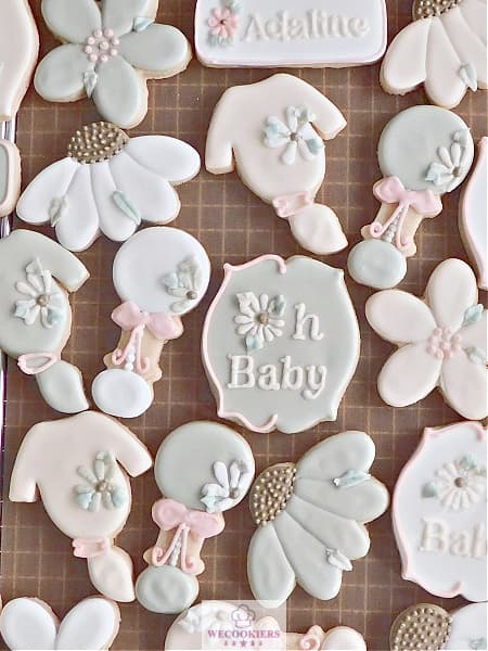 This image shows decorated baby girl cookies for showers. This is a mix of older and newer cutters designed in a neutral tone. See these baby girl shower cookies for inspo and techniques. See the most popular ones and view my royal icing transfer templates for baby girls too!