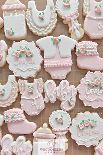 This image reflects soft pink and white baby cookies. It shows an array of shapes like booties, baby words, onesies,s, and rattles. These pastel pink and white baby girl shower cookies were the perfect set to welcome the little miss. See more inspo, techniques, popular cutters, and RI transfer templates here!